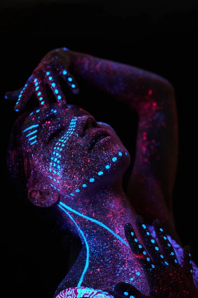Woman does yoga, hand movement, body warm-up. Art girl cosmos in ultraviolet light. Entire body is covered with colored droplets. Astral yoga. Noise, out of focus