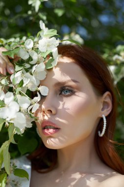 İlkbaharda çiçek açan elma çalılarının dallarında güzel bir kız. Parlak bir yaz gününde bir kadının portresi