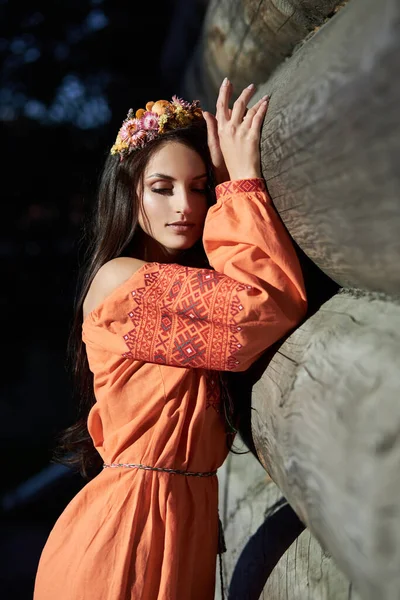 Beautiful Slavic woman in an orange ethnic dress and a wreath of flowers on her head. Beautiful natural makeup. Portrait of a Russian girl