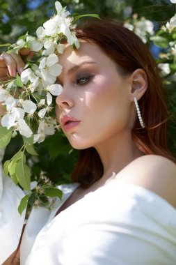 İlkbaharda çiçek açan elma çalılarının dallarında güzel bir kız. Parlak bir yaz gününde bir kadının portresi