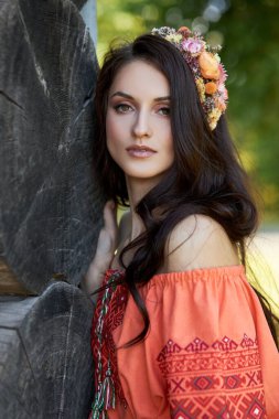 Turuncu etnik elbiseli ve kafasında çiçek çelengi olan güzel bir Slav kadın. Güzel doğal makyaj. Rus bir kızın portresi.