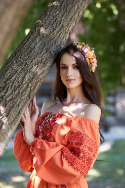 Turuncu etnik elbiseli ve kafasında çiçek çelengi olan güzel bir Slav kadın. Güzel doğal makyaj. Rus bir kızın portresi.