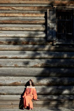 Turuncu etnik elbiseli ve kafasında çiçek çelengi olan güzel bir Slav kadın. Güzel doğal makyaj. Rus bir kızın portresi.
