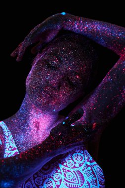 Sanat kadını ultraviyole ışıkta kozmos. Bütün vücudu renkli damlacıklarla kaplı. Karanlıkta poz veren kız. Gürültü, odak dışı