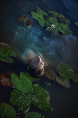 Genç bir kadın, sakin sularla çevrili nilüferlerle bezenmiş bir gölde huzur içinde yüzüyor. Sıcak bir öğleden sonra sakin ve huzurlu bir anı yakalıyor..