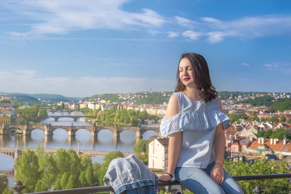 黑发女孩穿着休闲 坐在围栏上 享受太阳和伏尔塔瓦河河的看法在布拉格城市 捷克共和国 — 图库照片
