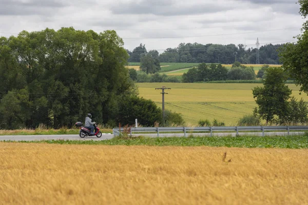 Man driving a scooter on the road through the agricultural fields, near the city Schwabisch Hall, Germany