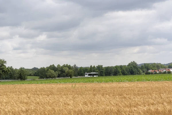 農地と森林に囲まれた小さなドイツ村に向かってドライブする公共交通機関バスと田舎の風景 — ストック写真