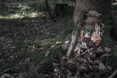 Korkuluk yaşlı bir ağaç kökleri arasında oturan bir ağaç dalı, yanında ile kurutulmuş yaprakları, karanlık bir orman kaplı. Cadılar Bayramı için bağlam.