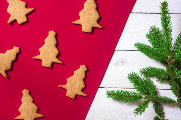 Minimalist Christmas image with ginger cookies in shape of an Xmas tree on a red background and a green fir twig on a white background.