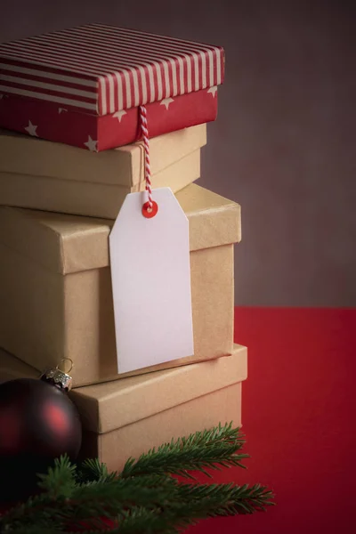 Xmas gifting image with a stack of gift boxes, an unwritten etiquette, fir twig, and a red Christmas ball, on a red background.