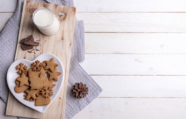 Noel kahvaltı masası gingerbread çerezleri bir plaka, kalp şeklinde çikolata ve sıcak süt, Beyaz ahşap bir masa üzerinde ahşap bir tepside ile.