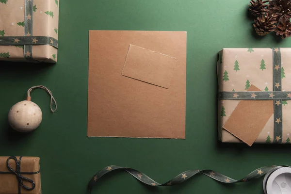 クリスマス プレゼントや装飾品に囲まれた 緑の背景に書き込まれていないヴィンテージの茶色の紙 — ストック写真