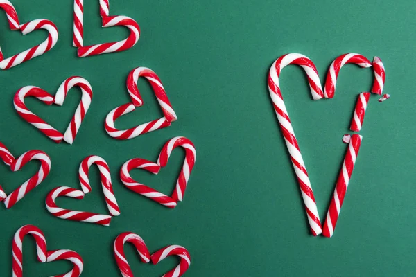 Red and white mini candy canes, arranged in heart shapes, and big candy canes in the shape of a broken heart, on a green background.