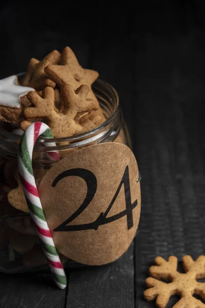 Kağıt etiket sayı 24 üzerinde tam bir cam kavanoz ile ev yapımı gingerbread çerezleri ve kırmızı-yeşil soyulmuş şeker kamışı ile