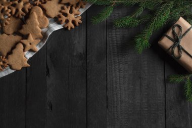 Noel kurabiyeleri yüksek açı bakış bir mutfak havlusu, köknar dal ve siyah ahşap bir masa üzerinde bir yay ile kahverengi hediye. Noel gelenekleri bağlam.