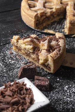 Dikey görüntü bir dilim elmalı turta bıçak, Bütün lezzetli pasta arka planda siyah bir tabloda çikolata ve pudra şekeri.