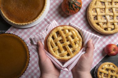 Bir havlu üzerinde çeşitli kekler, Kabak börek ve elmalı turta, dolu bir mutfak masasının üzerinde bir elmalı turta tepsisiyle holding eller. Ev pişmiş pasta.