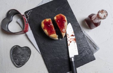 Tasty homemade heart-shaped raspberry cake sliced in two on a cutting board. Strawberry sauce poured over the cake. Directly above view with the kitchen table
