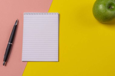 Görünüm boş defter sayfası, bir kalem ve bir yeşil elma ile renkli ofis masası ile yukarıda.
