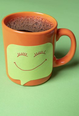 Bir yapışkan kağıt Not ile kahve fincan sıcak. Turuncu fincan kahve sabit yeşil bir yapışkan not Not olarak çizilmiş gülen yüz