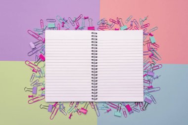 Boş açık defter ve büro malzemeleri, kağıt kıskaçları, klipler ve itme çivi çok renkli bir arka plan üzerine çok sayıda