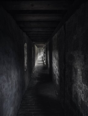 Weathered passageway in low light, in a medieval building, with beams of light. A long hallway in shadow with light at the end. Vintage architecture.