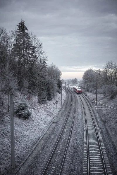 Rail tracks and German passenger train traveling through snowy nature, in a cold morning of December. Railway infrastructure. Public transport.