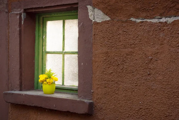 古い家から窓枠に緑色の花瓶の黄色い春の花 — ストック写真