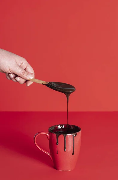 Melted chocolate dripping from wooden spoon. Mug with chocolate