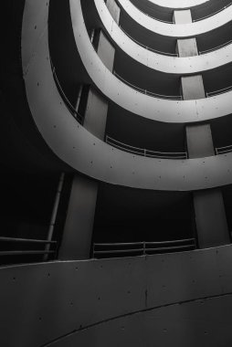 Yeraltı otoparkında, alt tarafı siyah beyaz. Beton duvarlı spiral otopark. Sütunları ve eğrileri olan soyut mimari