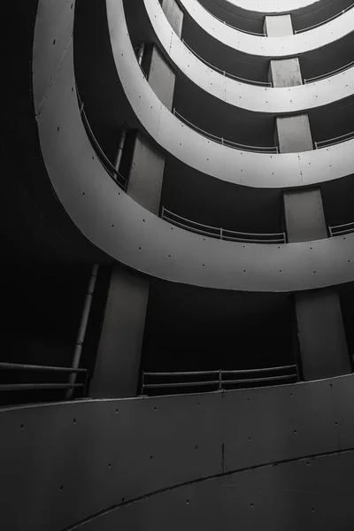 Yeraltı otoparkında, alt tarafı siyah beyaz. Beton duvarlı spiral otopark. Sütunları ve eğrileri olan soyut mimari