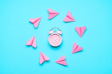 Pembe kağıt uçaklar ve mavi arka planda çalar saat ile zaman uçuşu kavramı. Son dakika gezisi. Zaman kavramı. Seyahat sembolü zamanı.