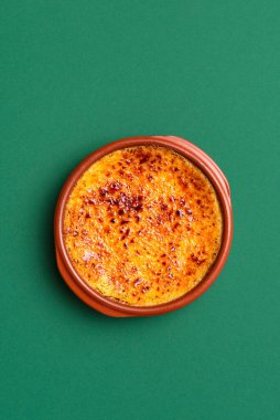 Yeşil dikişsiz arka planda, kil tepside karamel kabuklu ev yapımı creme brulee. Fransız kremalı pasta. Karamelli kahverengi şekerli yanmış krema.