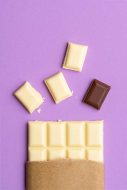 Beyaz çikolata parçaları ve mor bir arka planda izole edilmiş sütlü çikolata. Grup kavramından uzak dur. Düz çikolata çeşitleri.
