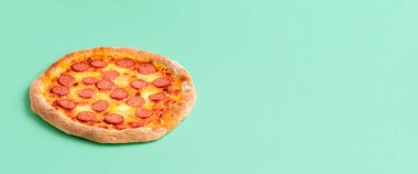 Mozzarella soslu pizza pepperonisi. Yeşil, pürüzsüz bir arka plan ve fotokopi alanı var. Sosisli geleneksel pizzanın tanıtım broşürü..