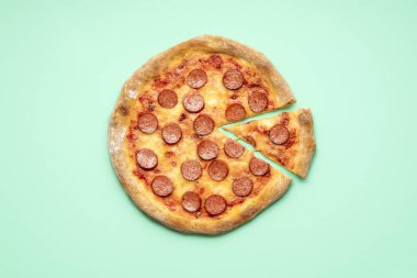 Yeşil nane arkaplanda pepperonili pizzayla yatıyordu. Tek dilim pizza pepperonili üst manzara. Mozzarella, sosis ve domates soslu ev yapımı pizza.