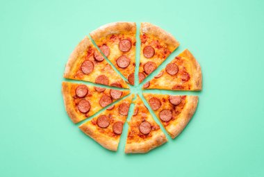 Yeşil arkaplanda izole edilmiş dilimlenmiş pepperonili pizza ile üst manzara. Ev yapımı pizza salamıyla yatıyordu..