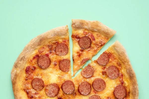 Top view with home-baked pepperoni pizza on a green-mint background. Slice of pepperoni pizza, above view. Freshly baked pizza with mozzarella, tomato sauce and sausages.