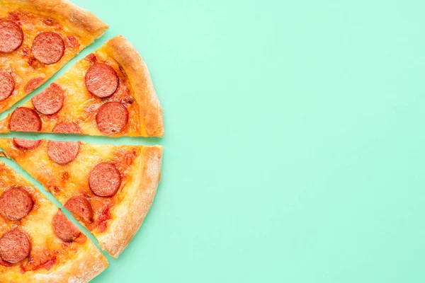 Yeşil arkaplanlı pepperonili pizzayla üst tarafta. Yeşil renkli bir masada dilimlenmiş pizza. Ev yapımı pizza.