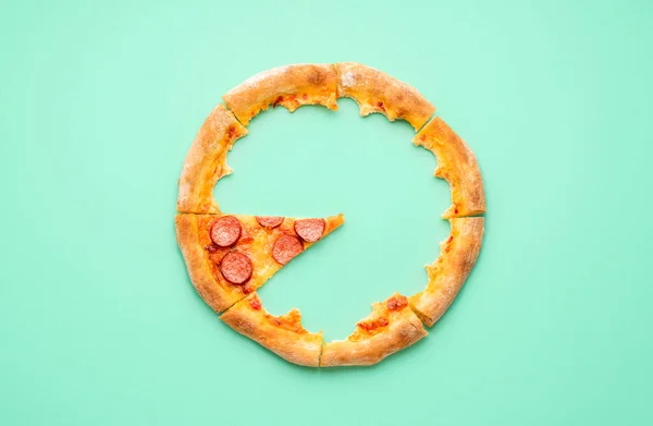 Kabuklu ve pepperonili pizzanın tek dilimli hâli. Yeşil arkaplanda pizza artıklarıyla üst manzara.