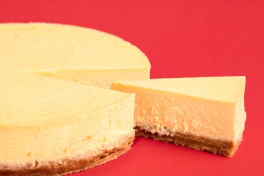 Cheesecake 'e yakın plan, bir dilim pasta ayrı duruyor, kırmızı arka planda izole edilmiş. Kremalı cheesecake dilimli makro. Noel yemeği tatlısı.