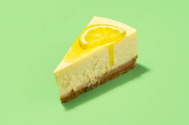 Limon soslu cheesecake dilimi ve yeşil arka planda izole edilmiş limon dilimi. Sarı şuruplu bir dilim peynirli keki yakından çek..