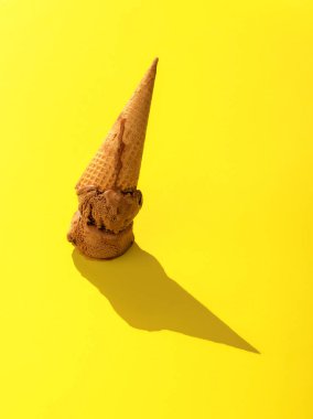 Sarı arka planda ters dönmüş waffle külahlı dondurma. Parlak ışıkta çikolatalı dondurmayla yakın plan..