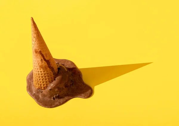 Waffle külahına çikolatalı dondurma düşürdüm, sarı, pürüzsüz bir zeminde eriyorum. Ters çevrilmiş dondurmaya yakın çekim. Yaz dondurulmuş tatlı.