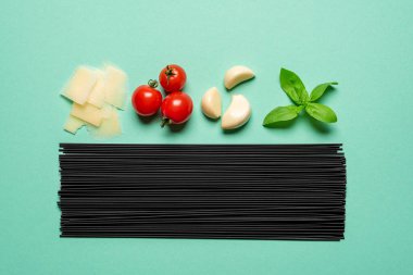 Pişmemiş siyah spagetti ve domates sosu için malzemeler, yeşil bir masanın üst manzarası. Lezzetli bir İtalyan yemeği için ham malzemeler, domates soslu spagetti..