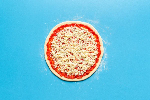 Yukarıdaki pizzanın mavi renkli bir masa üzerindeki görüntüsü. Domates soslu pizza hamuru ve mozzarella üstü manzaralı. Ev yapımı klasik geleneksel pizza..