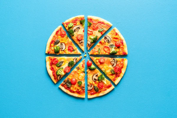 Top view with a sliced pizza primavera on a blue table. Vegetarian pizza flat lay. Sliced pizza isolated on a blue colored background.