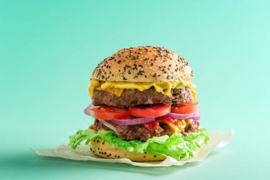 Yeşil renkli bir masada ev yapımı hamburger. Balmumu bir bez parçasına hamburger. Yeşil arka planda büyük bir çizburger minimalisti.
