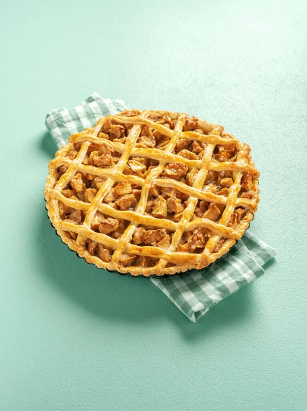 Freshly baked apple pie on a kitchen towel in bright light. Lattice crust tart with apple filling minimalist on a green colored table.
